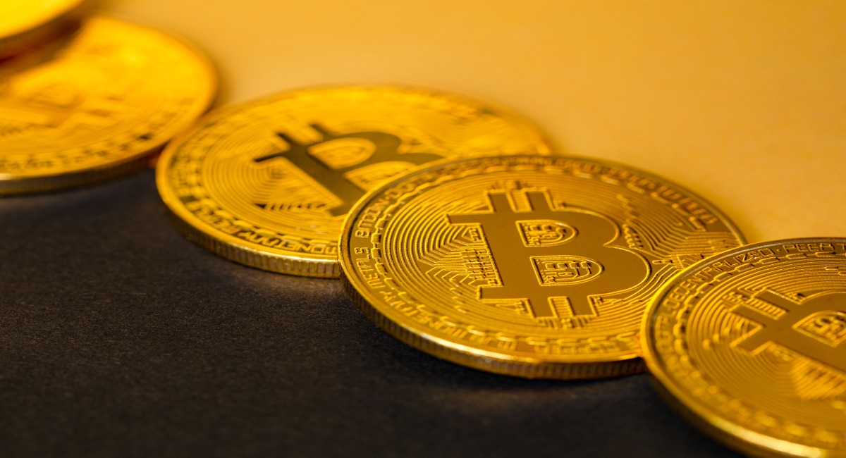 Closeup of shiny bitcoin cryptocurrency arranged on gold and black background.